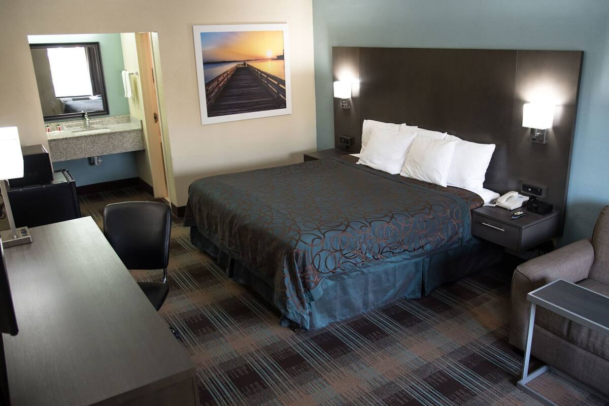 Habitación de hotel con cama, escritorio, silla, mesita de noche con teléfono y lámpara de pared.