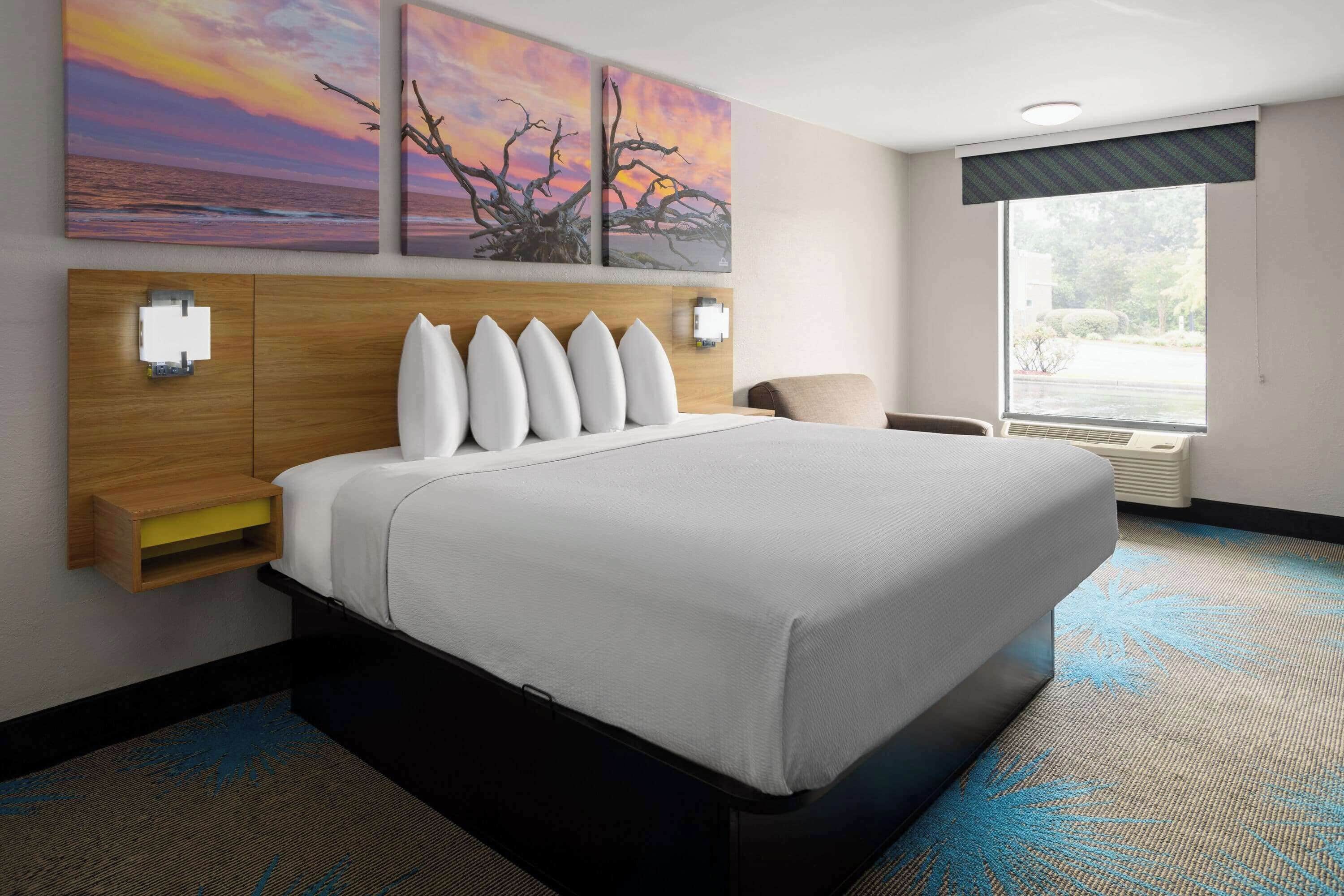 A hotel room with a large bed, a wooden headboard, wall-mounted lights, and a window with a view of the outdoors.