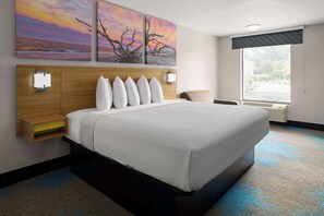 Habitación de hotel con una cama grande, cabecera de madera, luces fijadas a la pared y ventana con vistas al exterior.