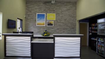 Zona de recepción con pared de piedra, ventilador de techo, computadora Dell, refrigerador con bebidas y un arreglo floral.