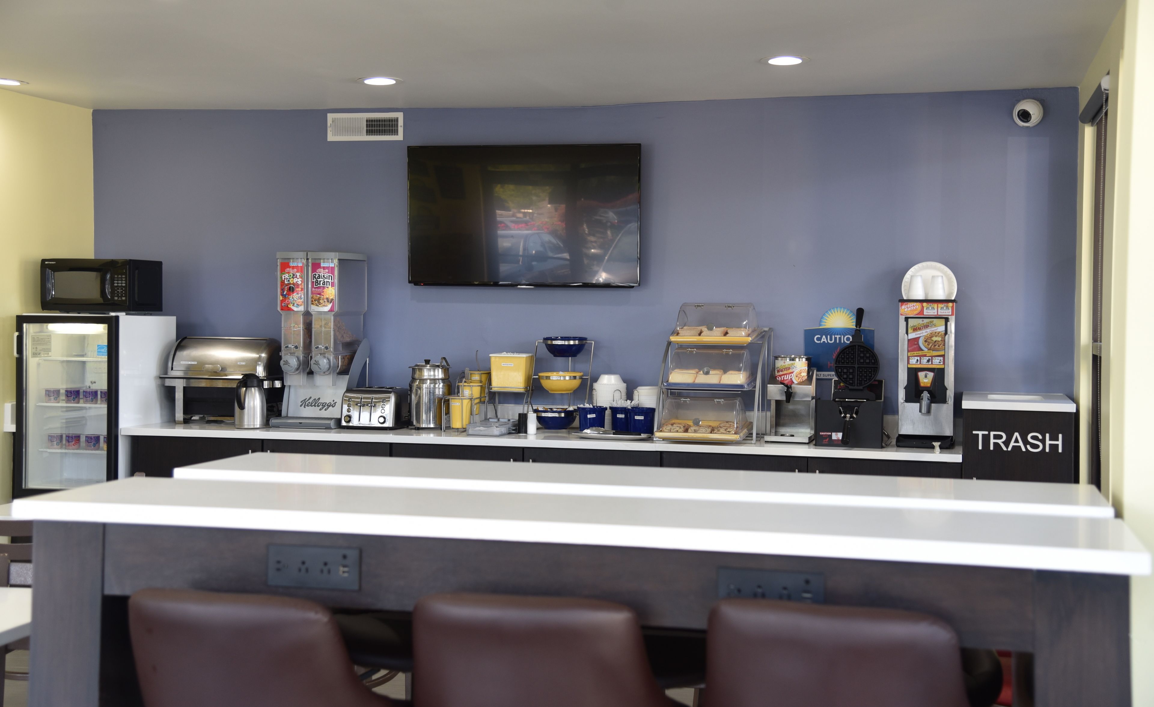 A self-service breakfast bar with various food and drink dispensers, a microwave, and a trash bin.