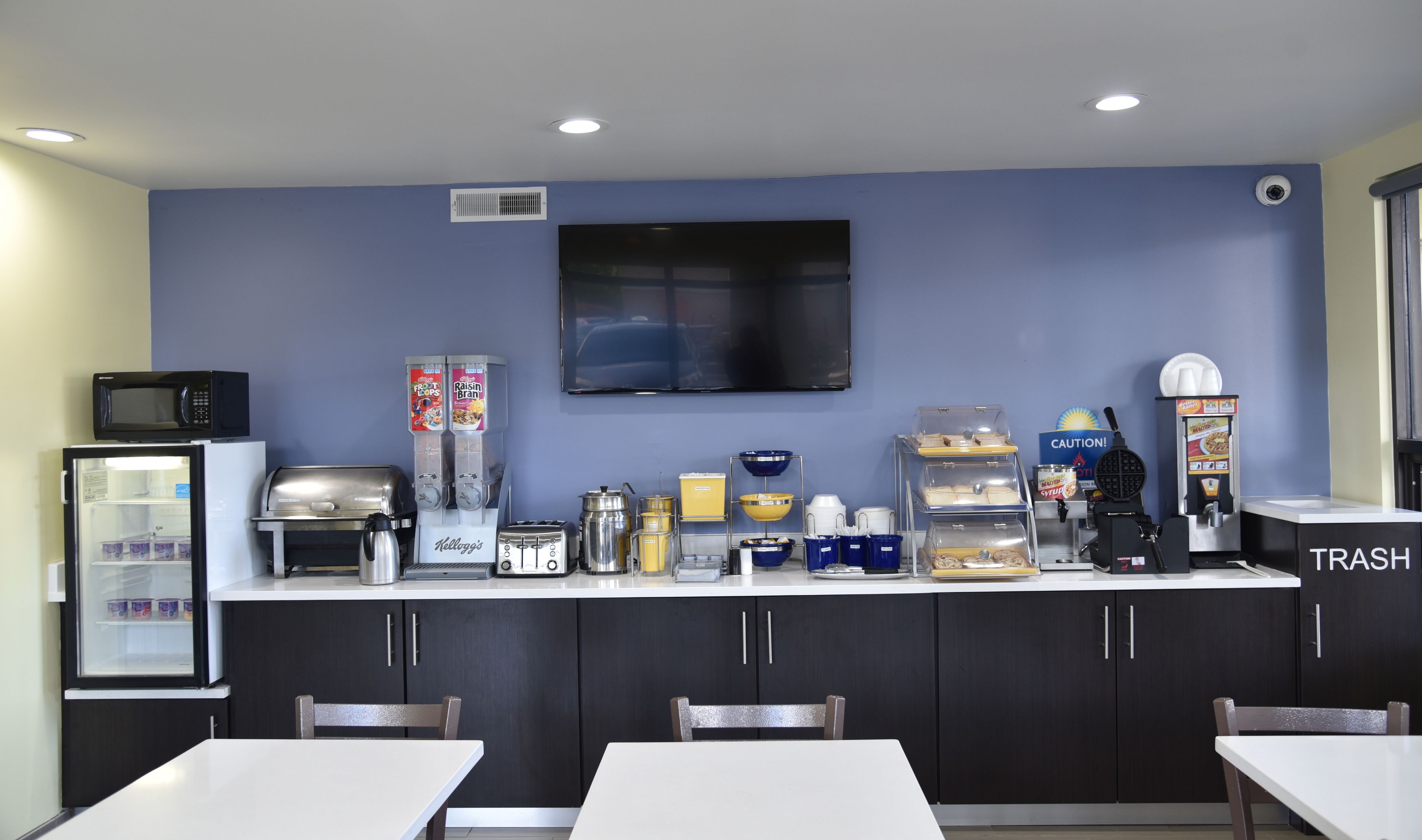 A kitchenette with a microwave, refrigerator, toaster, coffee machine, and a trash bin.