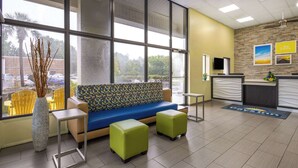A reception area with a blue sofa, green ottomans, and a patterned vase.