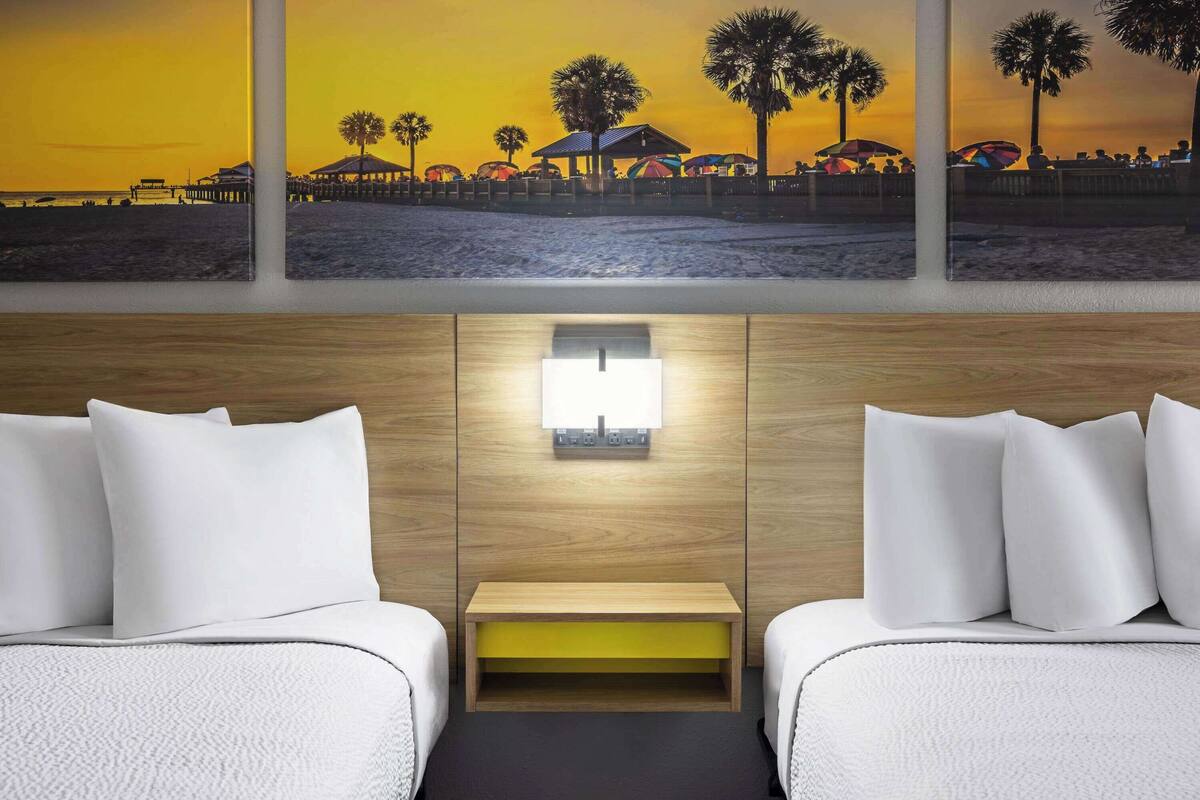 Habitación de hotel con dos camas, una mesita de noche, una lámpara de pared y una pintura de una escena de playa sobre las camas.
