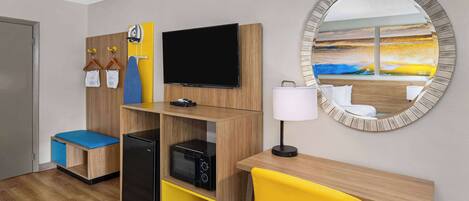 A hotel room with a wooden desk, a television, a mirror, and a seating area with a yellow chair.