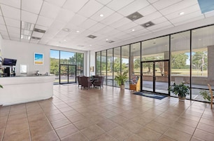 A spacious lobby with a reception desk, seating area, and large windows offering views of the outdoors.