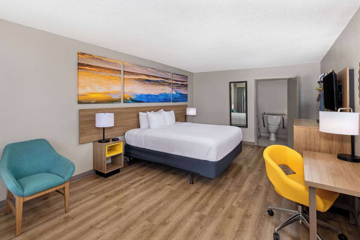 A hotel room with a bed, a desk, a chair, a bathroom, and a painting on the wall.