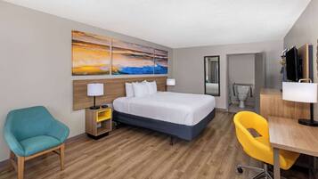 A hotel room with a bed, a desk, a chair, a bathroom, and a painting on the wall.