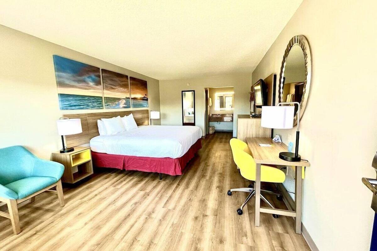 A hotel room with a bed, a desk, a chair, a mirror, and a painting on the wall.