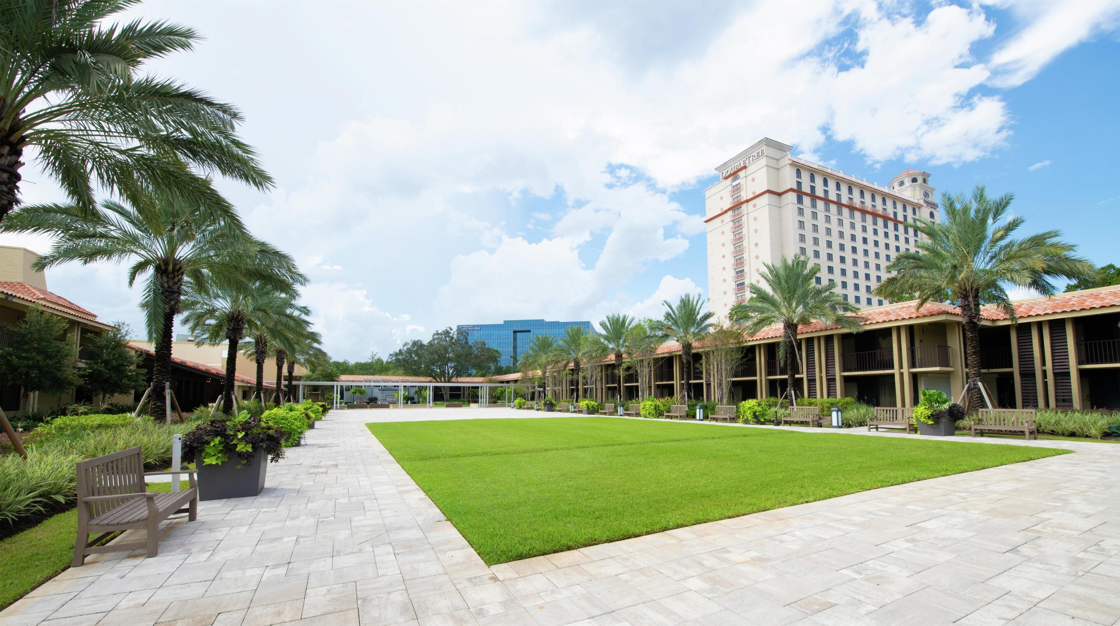 A hotel courtyard with a green lawn, palm trees, and a building with a red roof.