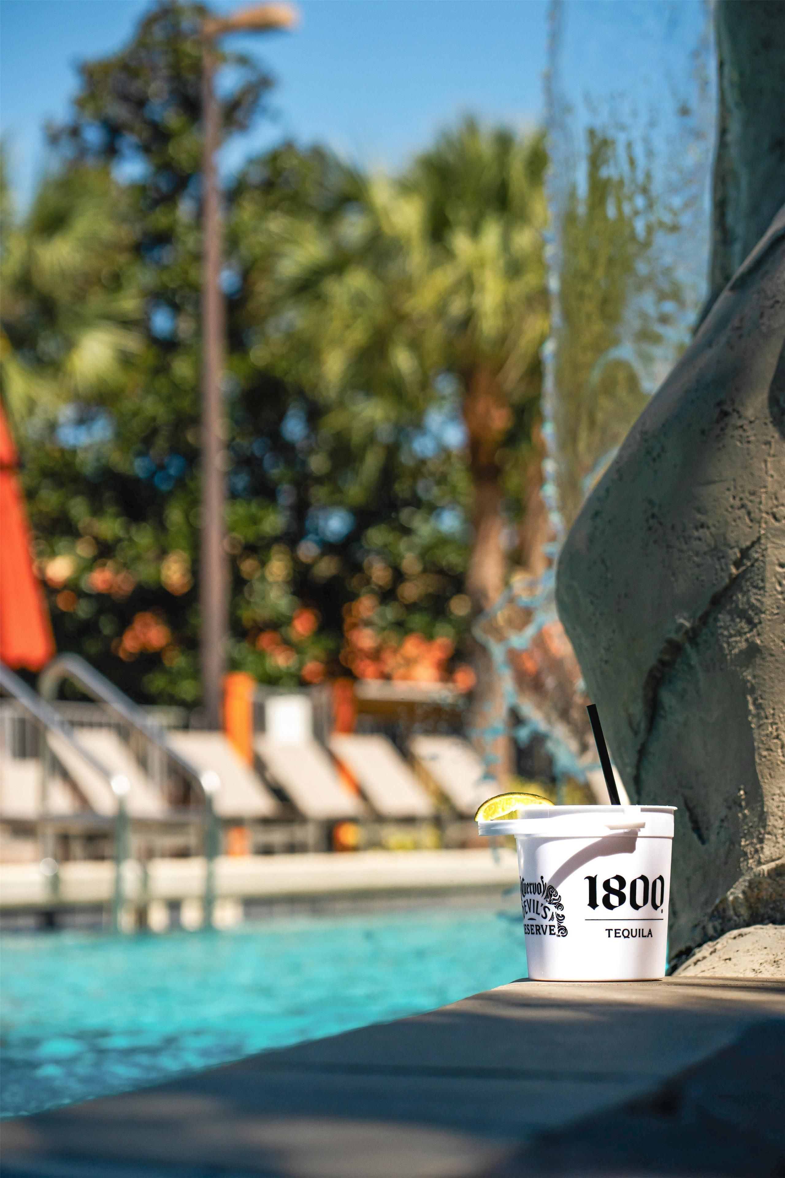 A poolside setting with a drink cup labeled '1800 Tequila' and a pool with clear blue water.