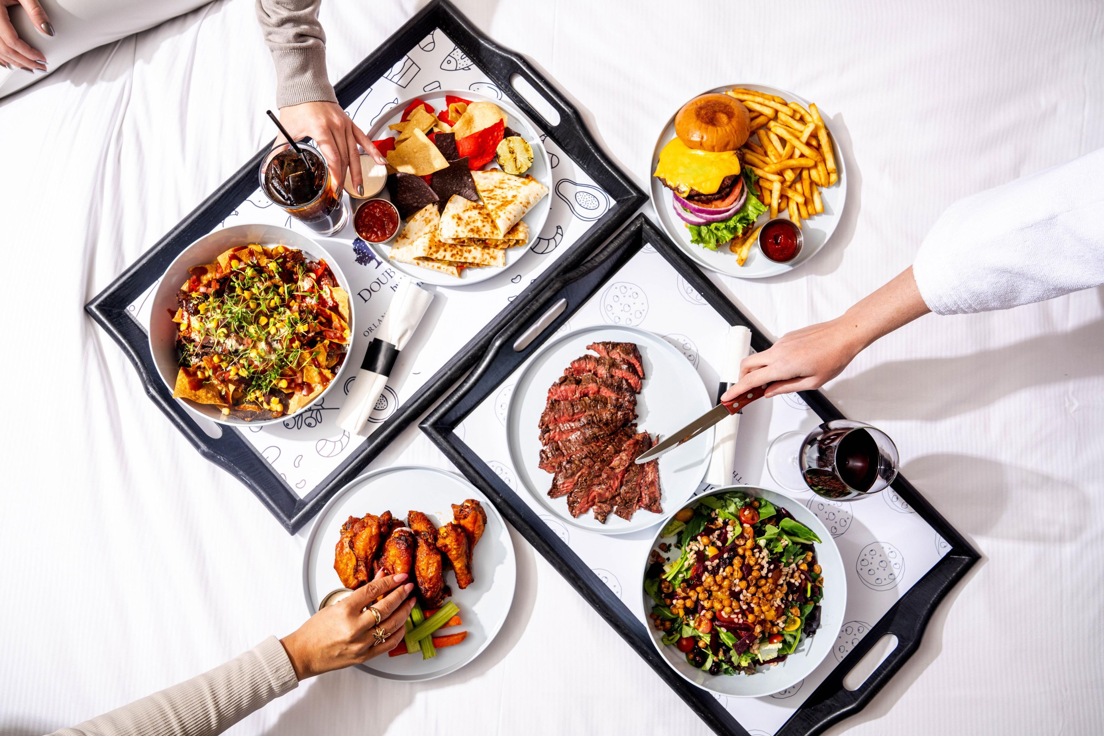 A dining table with various dishes including nachos, steak, wings, a burger, fries, and a salad.
