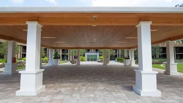 An outdoor covered area with a tiled floor, white columns, and a wooden ceiling.