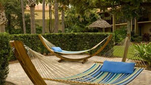 A hammock set up on a paved patio with a thatched roof structure in the background.