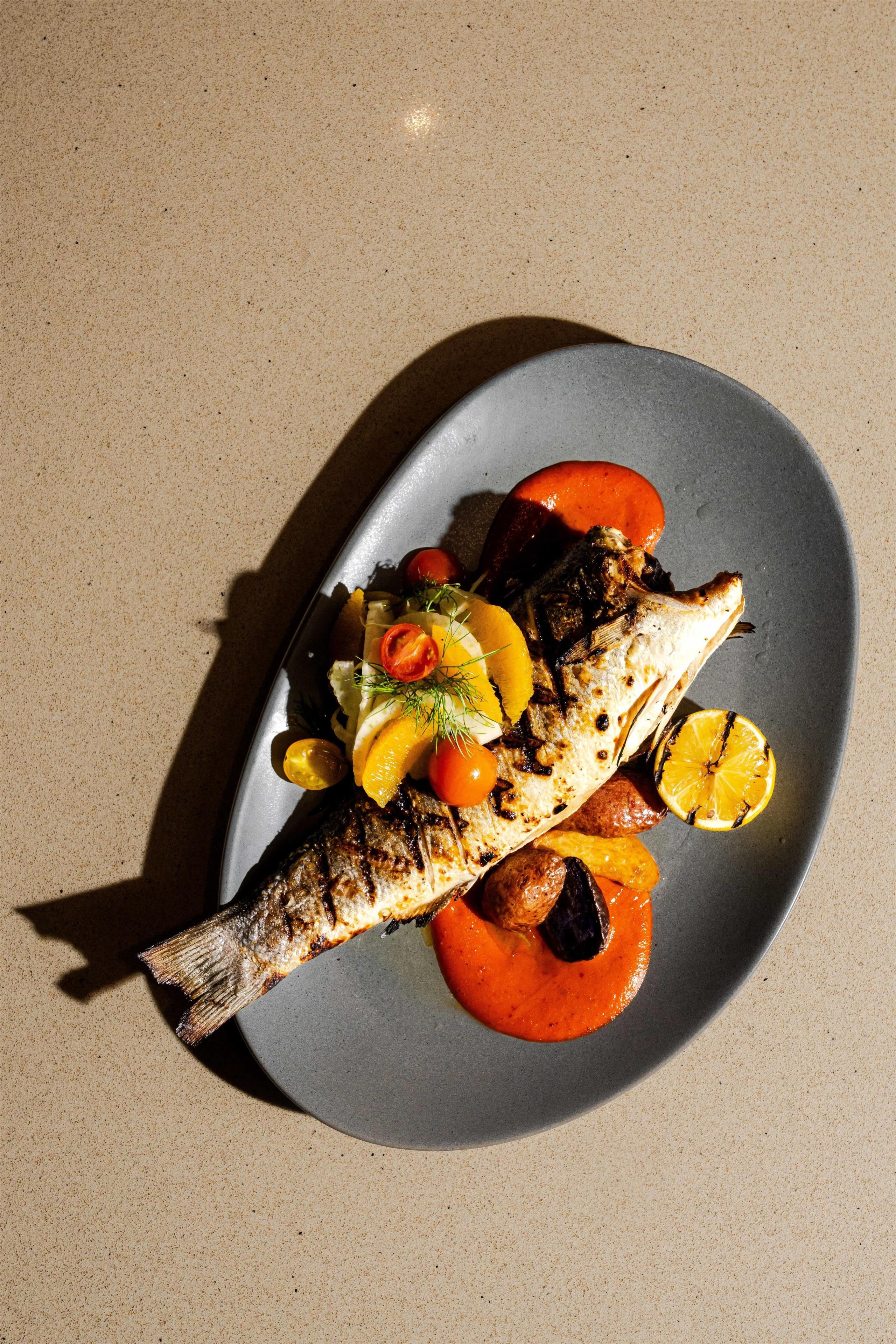 A plate with grilled fish, vegetables, and a sauce.