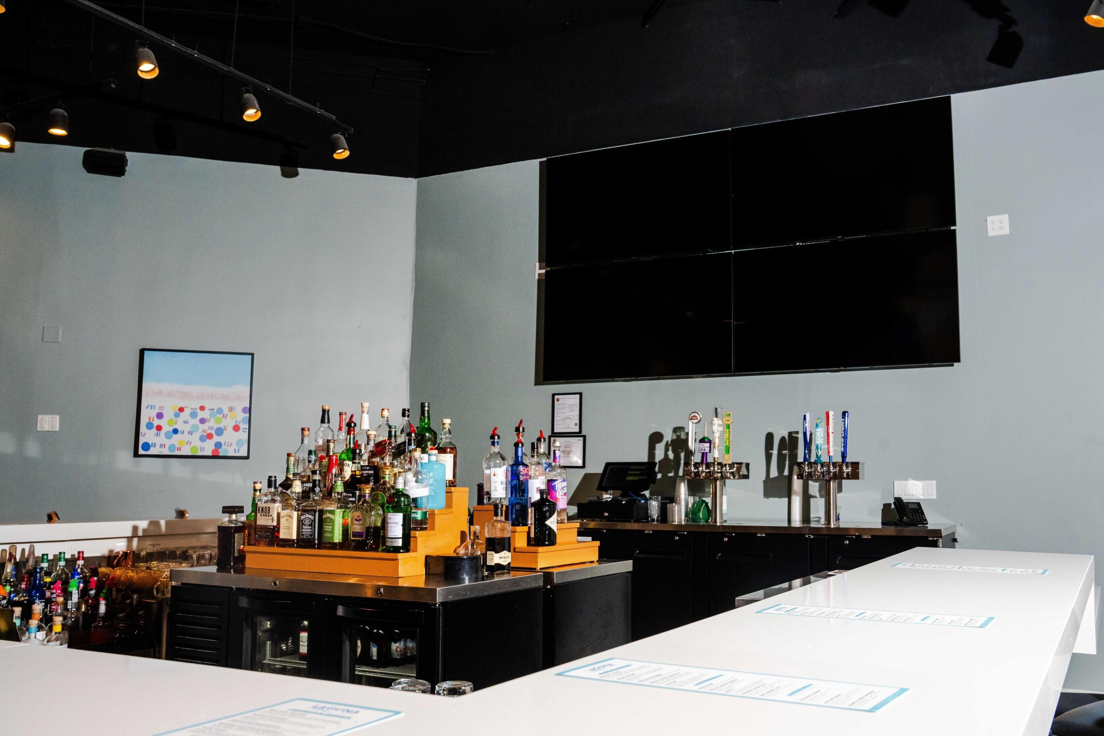 Un espace bar avec un assortiment de bouteilles, une caisse enregistreuse et une grande fenêtre.