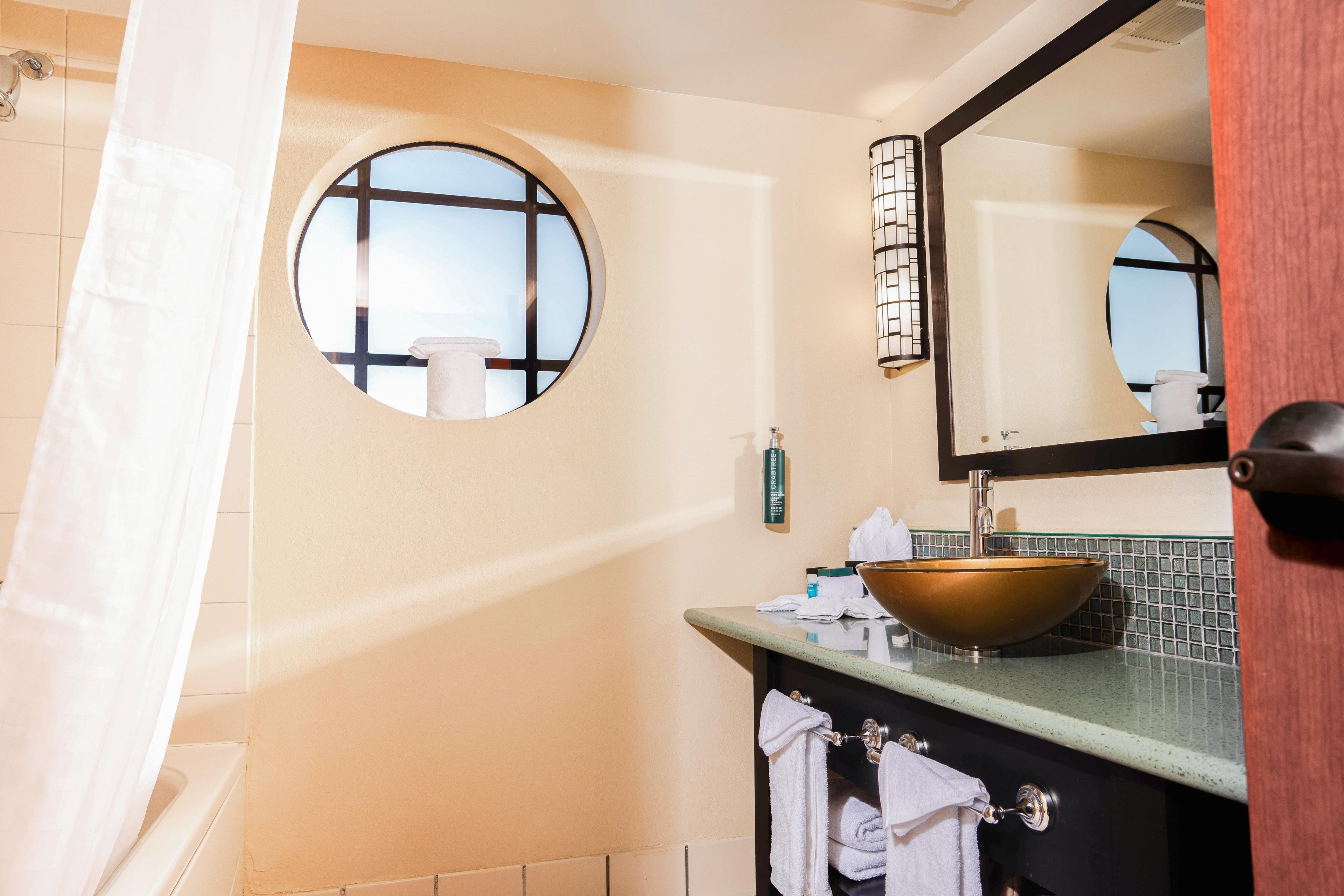Un baño con un espejo redondo, un lavabo con pileta y un perchero para toallas.