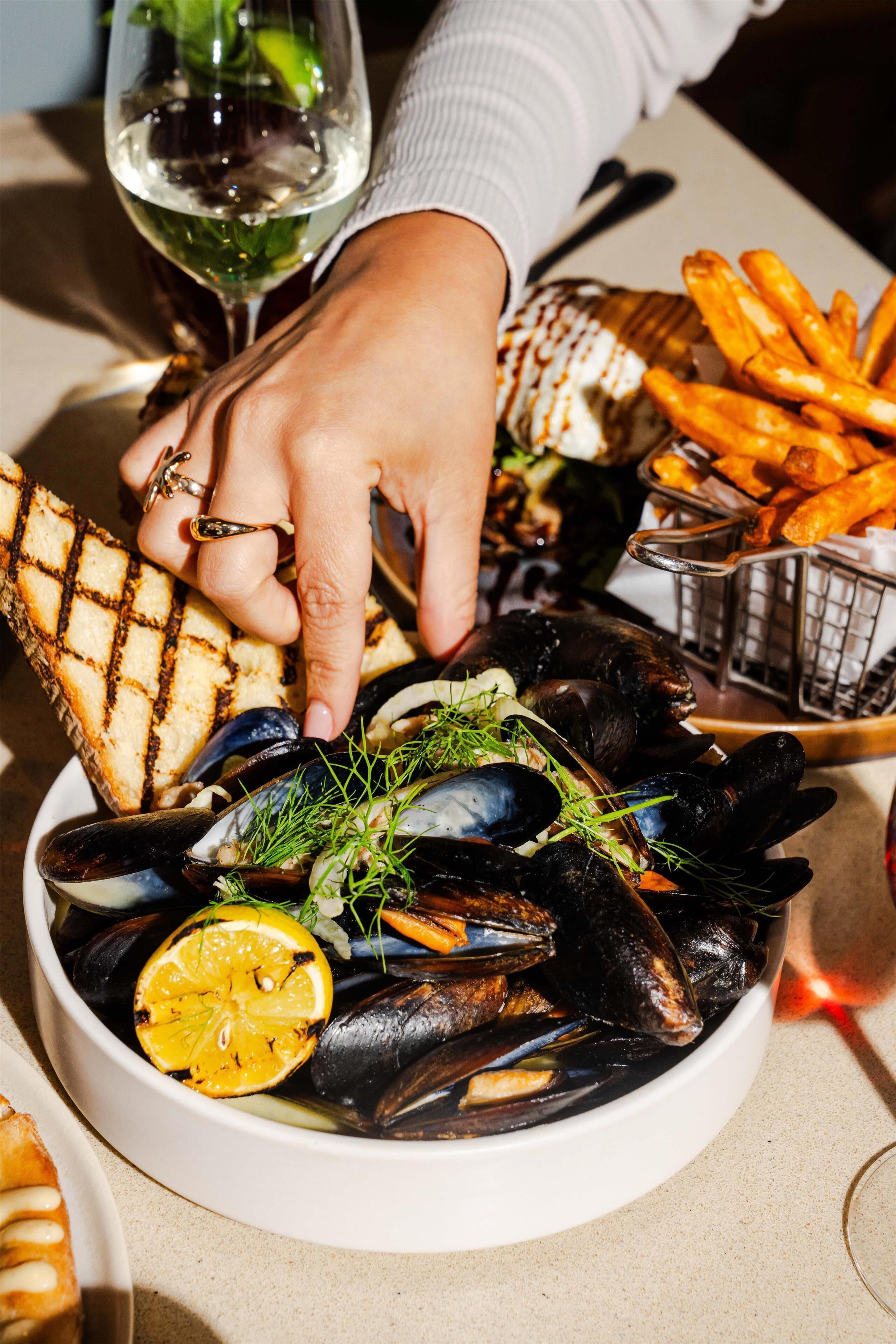 Eine Schüssel mit Muscheln, garniert mit Kräutern und Zitrone, dazu gegrilltes Brot und Pommes.