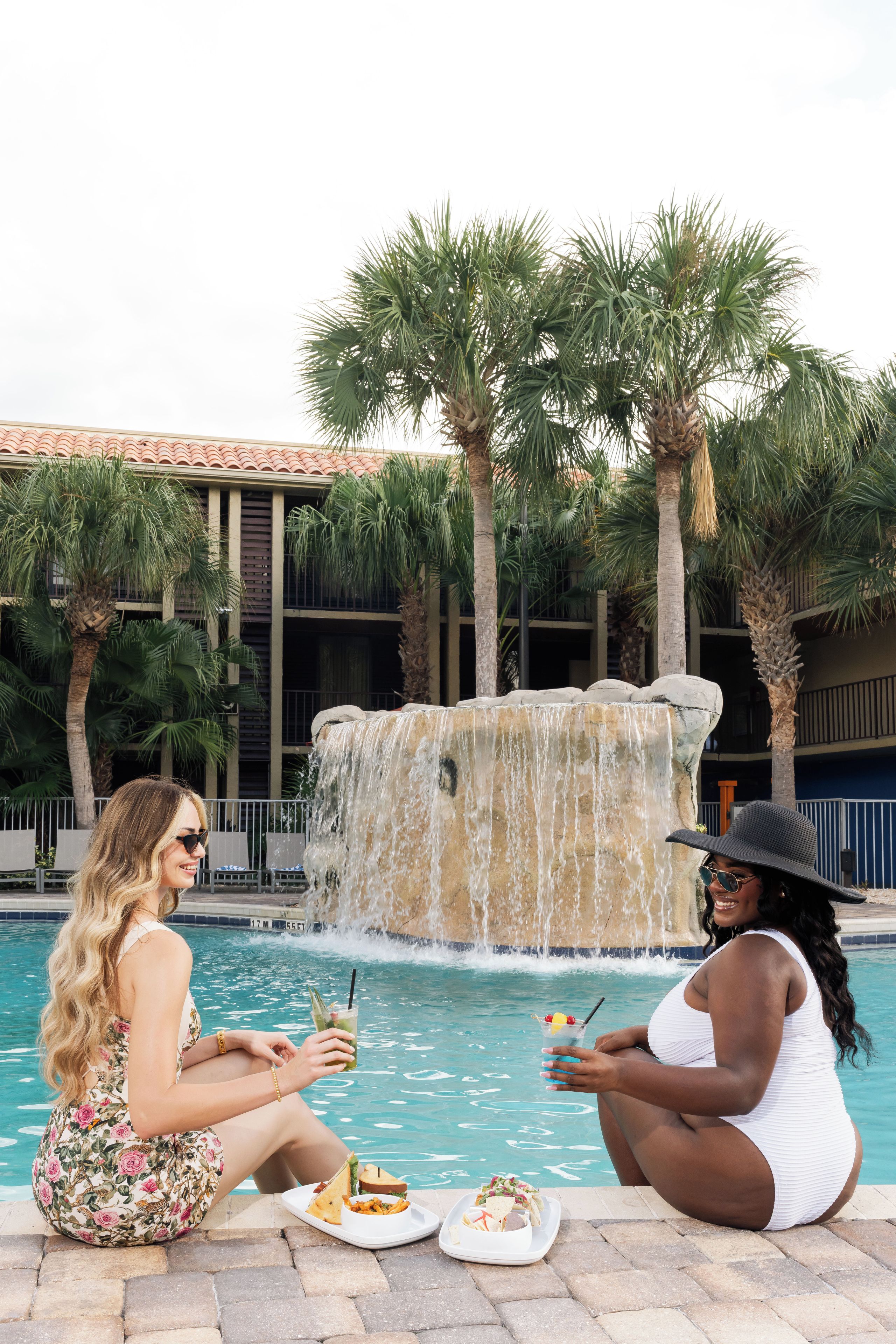 Two individuals seated by a pool with a waterfall feature in the background.