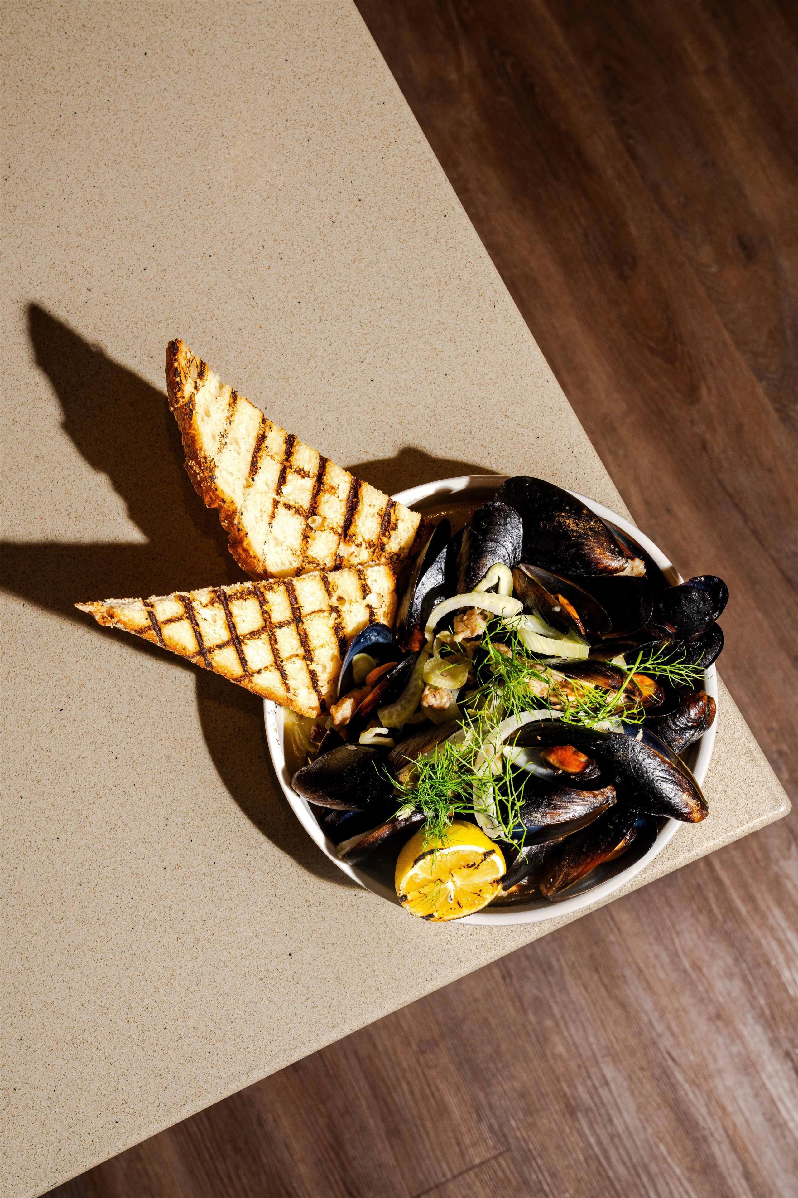 Un plato de mejillones a la parrilla con limón y hierbas, acompañado de pan tostado.