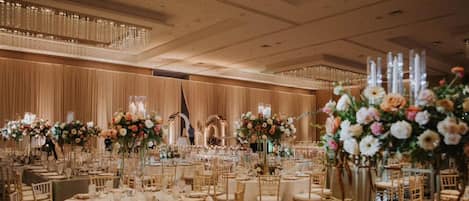 Un salón de banquetes con mesas redondas, sillas y centros de mesa florales.