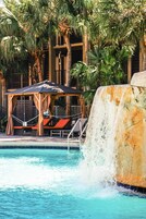Una piscina con cascata, circondata da palme e poltrone da relax.