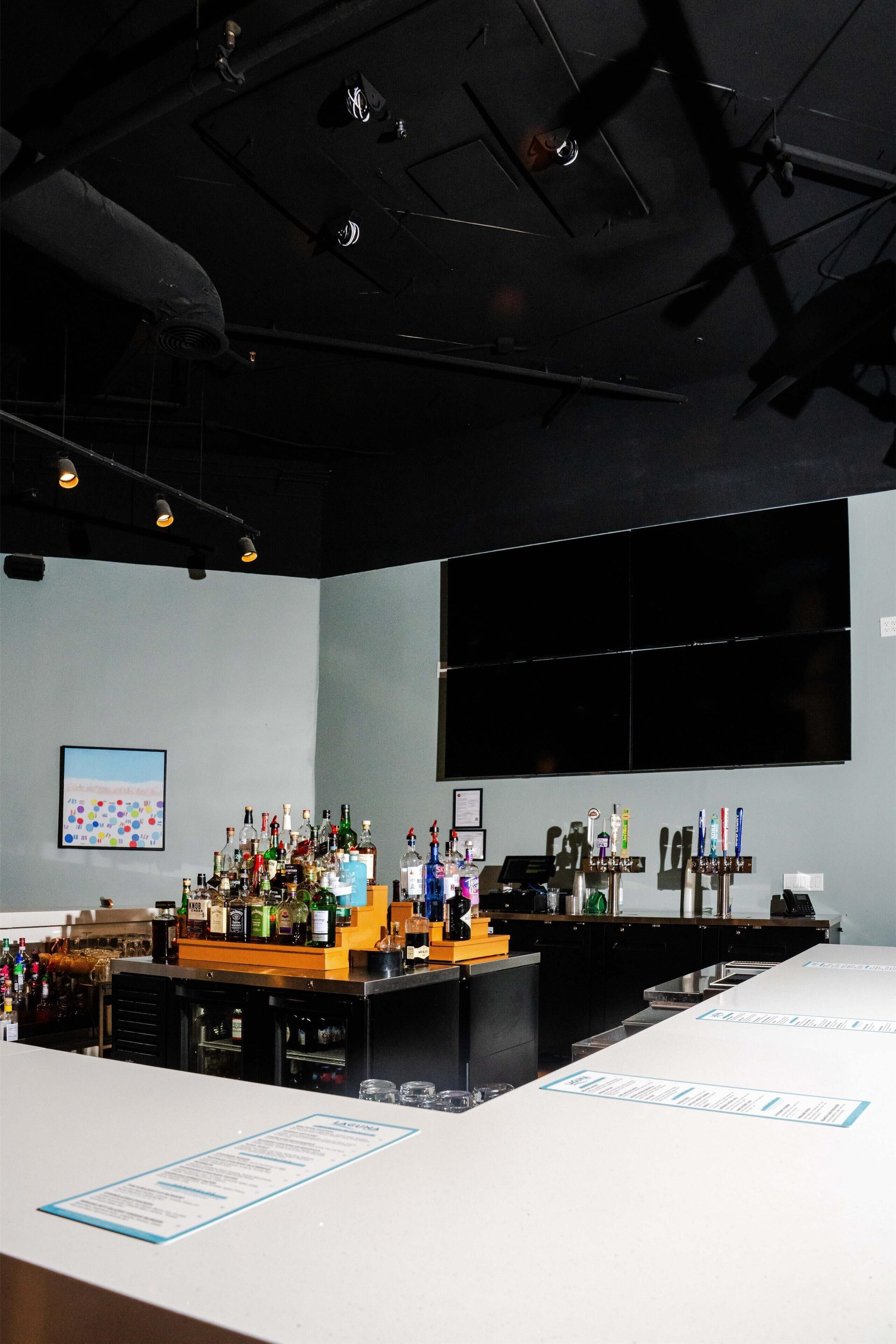 A bar area with a long counter, various bottles, and a menu stand.