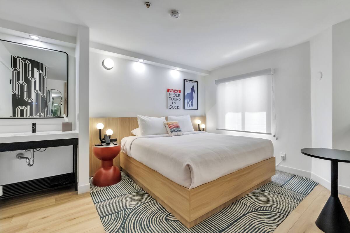 A modern bedroom with a wooden bed, a round red nightstand, a large mirror, and a small round table.