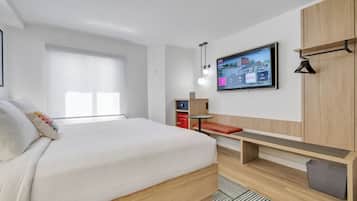 A modern hotel room with a large bed, a TV mounted on the wall, a small desk, and a bench.