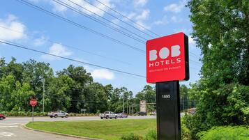 Ein Schild von Bob Hotels mit einer Botschaft zu günstigen Preisen, an einer Straßenkreuzung in der Nähe eines Stoppschilds.
