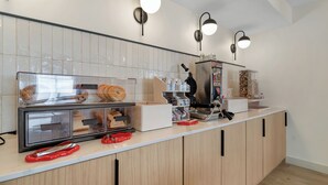 A kitchen with a counter, a bread display, a waffle maker, and a coffee machine.