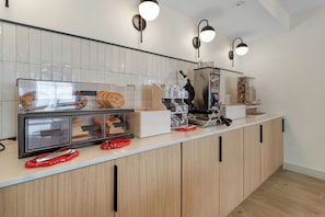 A kitchen with a counter, a bread display, a waffle maker, and a coffee machine.