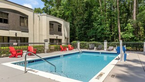 A rectangular pool with a metal ladder, surrounded by a white deck. Red chairs are placed along the pool's edge.