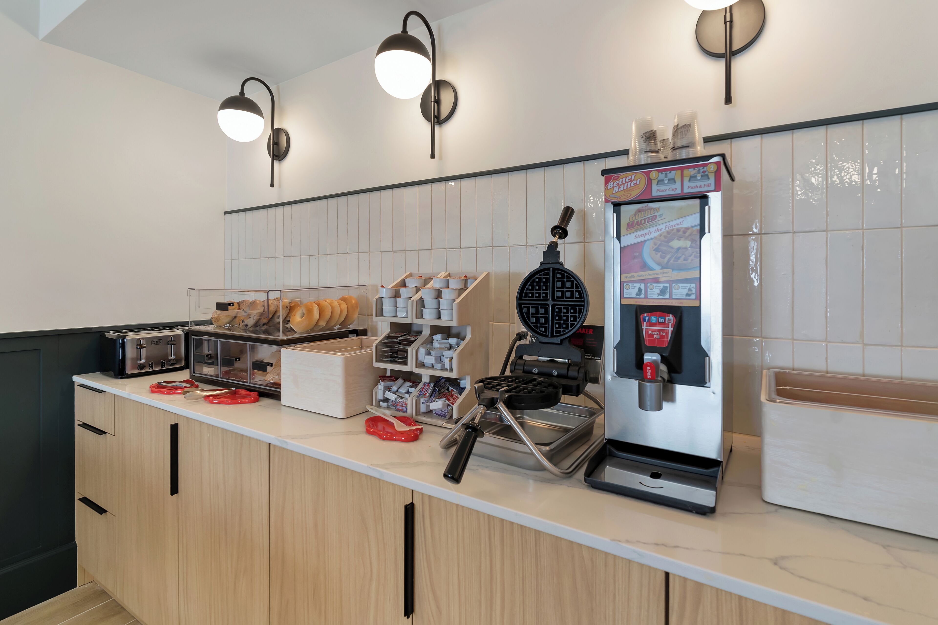 A kitchen counter with a waffle maker, toaster, and bread basket.