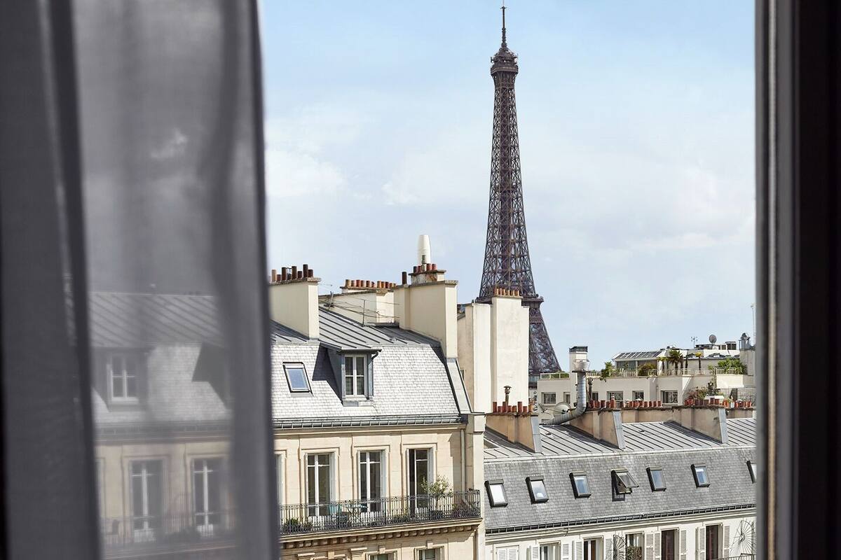 En vy över Eiffeltornet från ett fönster med utsikt över Paris taklandskap.