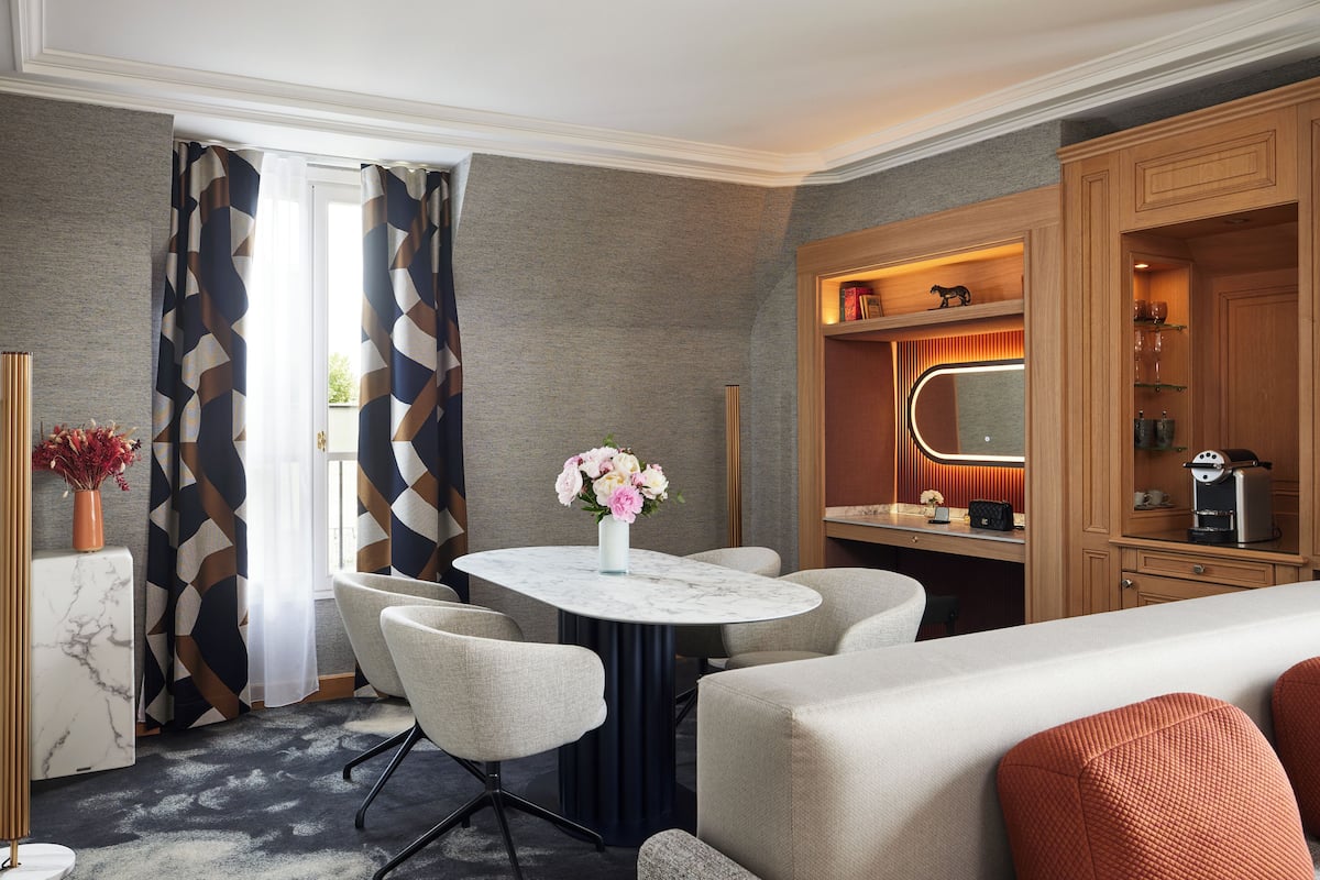 Ett hotellrum med ett runt bord i marmor, fyra stolar, en soffa, en minibar och en spegel.