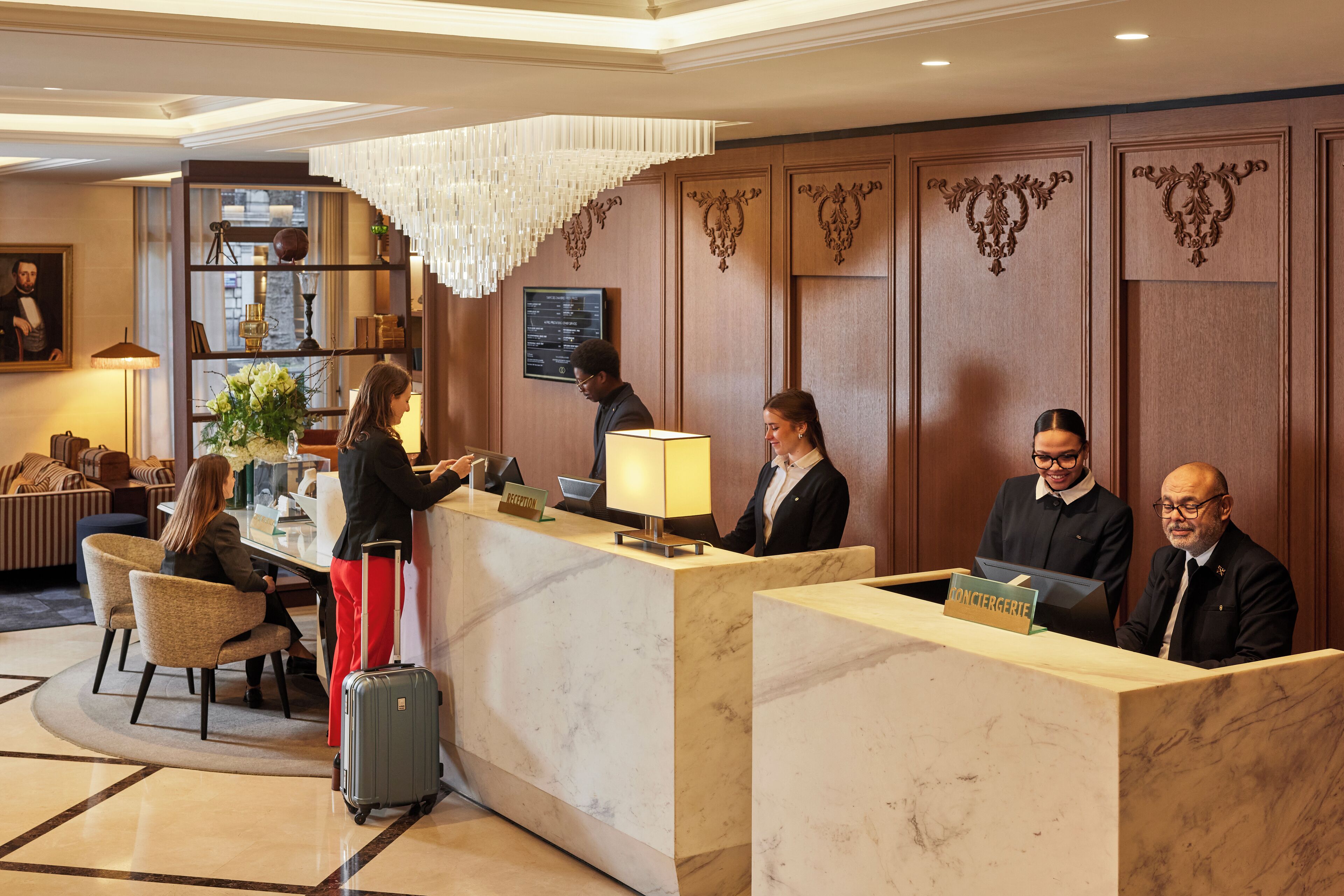 Un hall d’accueil d’hôtel avec des comptoirs en marbre, un lustre et un bureau d’accueil.