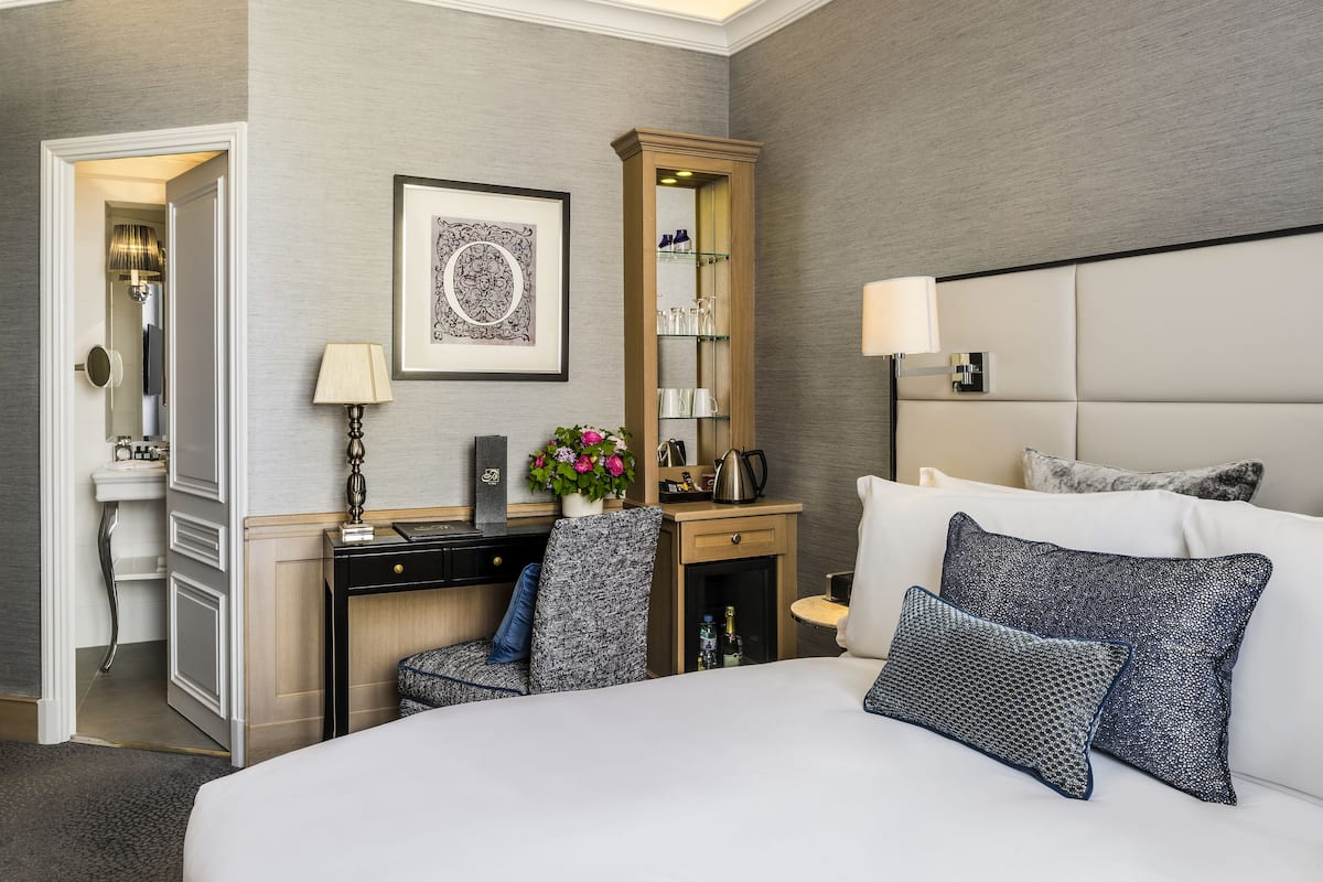 Ett hotellrum med en stor säng, ett skrivbord med en dator, en stol, ett litet skåp, en spegel och en vägglampa.