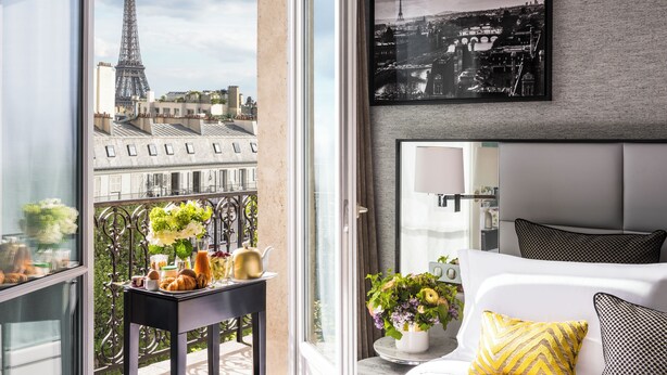 Een moderne hotelkamer met een groot raam met uitzicht op de Eiffeltoren, een stadsbeeld en een balkon met ontbijtartikelen.