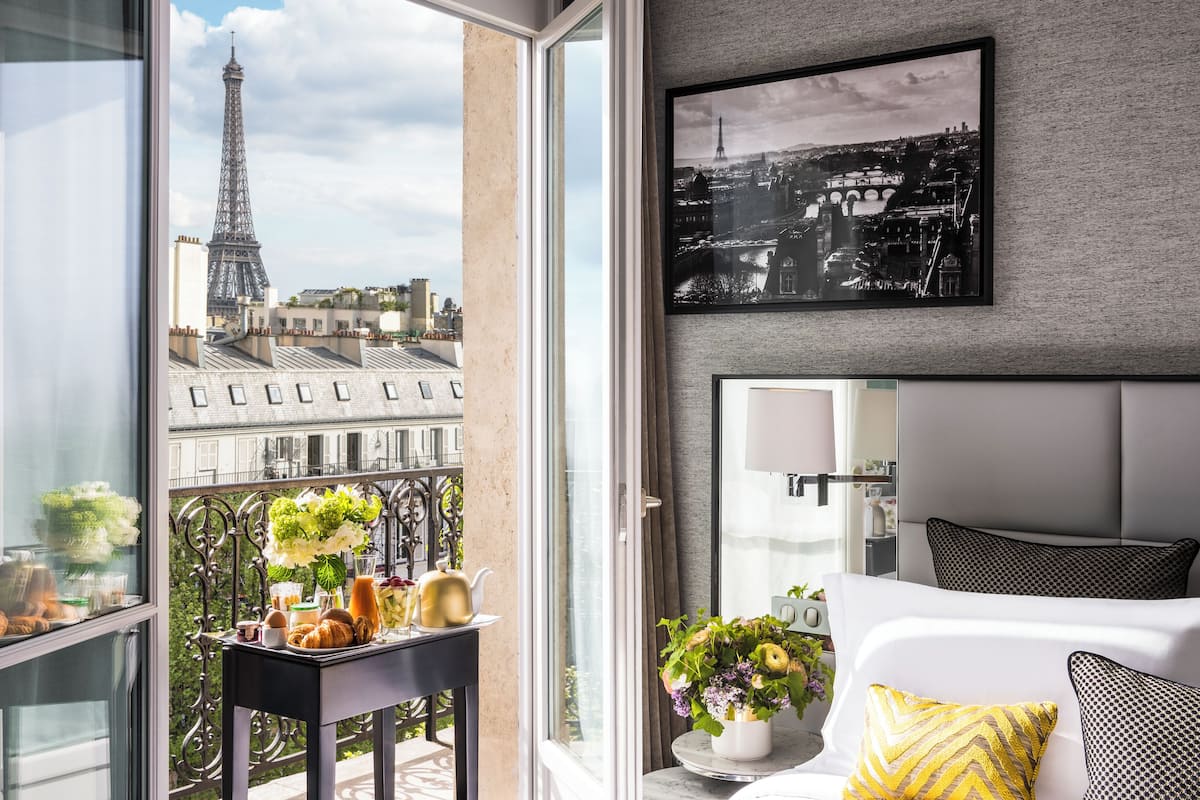Ett modernt hotellrum med ett stort fönster med utsikt över Eiffeltornet, en panoramautsikt över staden och en balkong där frukosten kan avnjutas.
