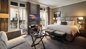 Een hotelkamer met een groot bed, een televisie, een bureau met stoel en een balkon met gordijnen.