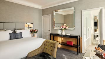 Ein Hotelzimmer mit einem großen Bett, einem Nachttisch mit Blumen in einer Vase, einem Spiegel, einem Holzkonsolentisch und einem roten Koffer.