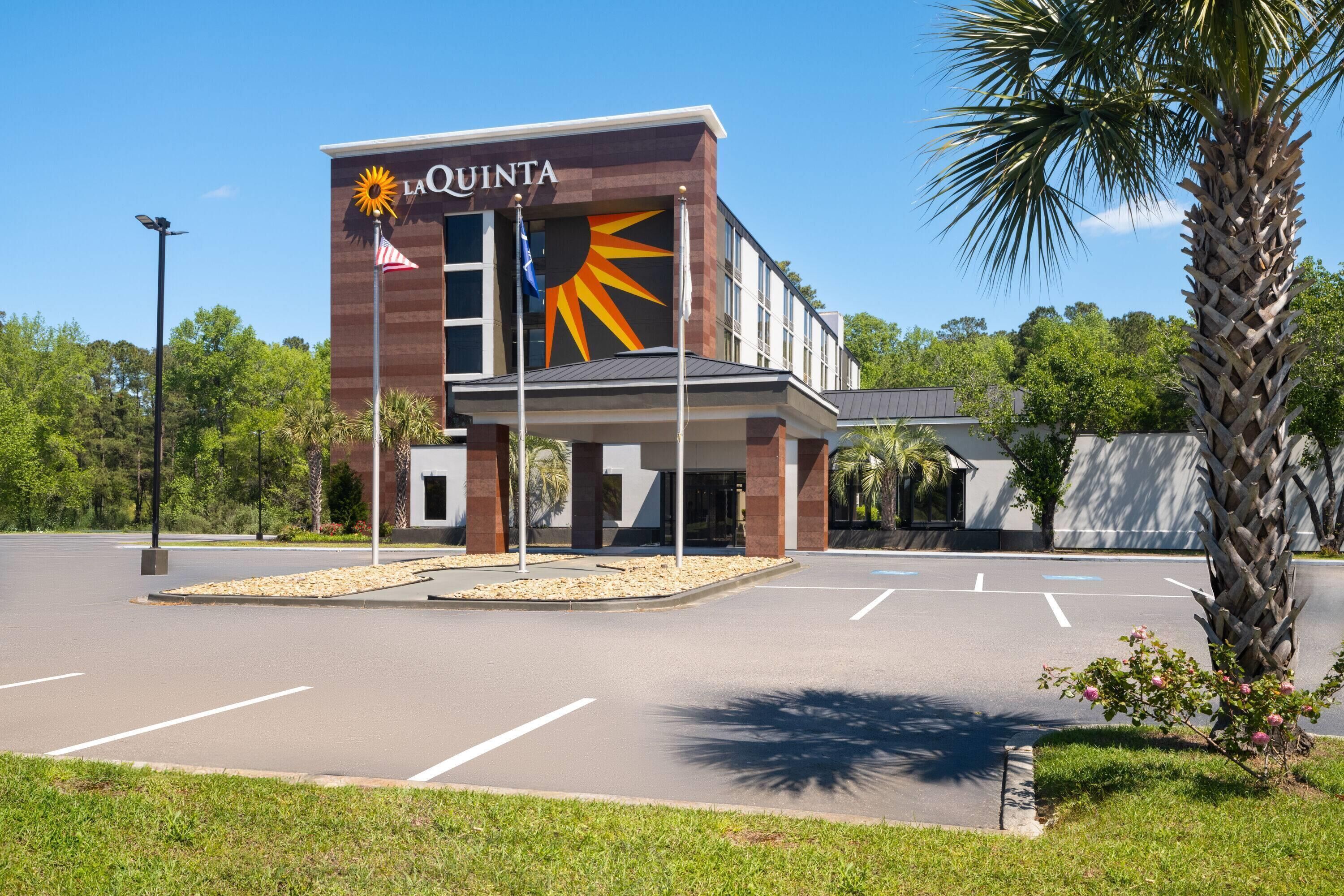 Et hotel ved navn La Quinta med en sol- og stjernelogo, en parkeringsplads og et palmetræ.