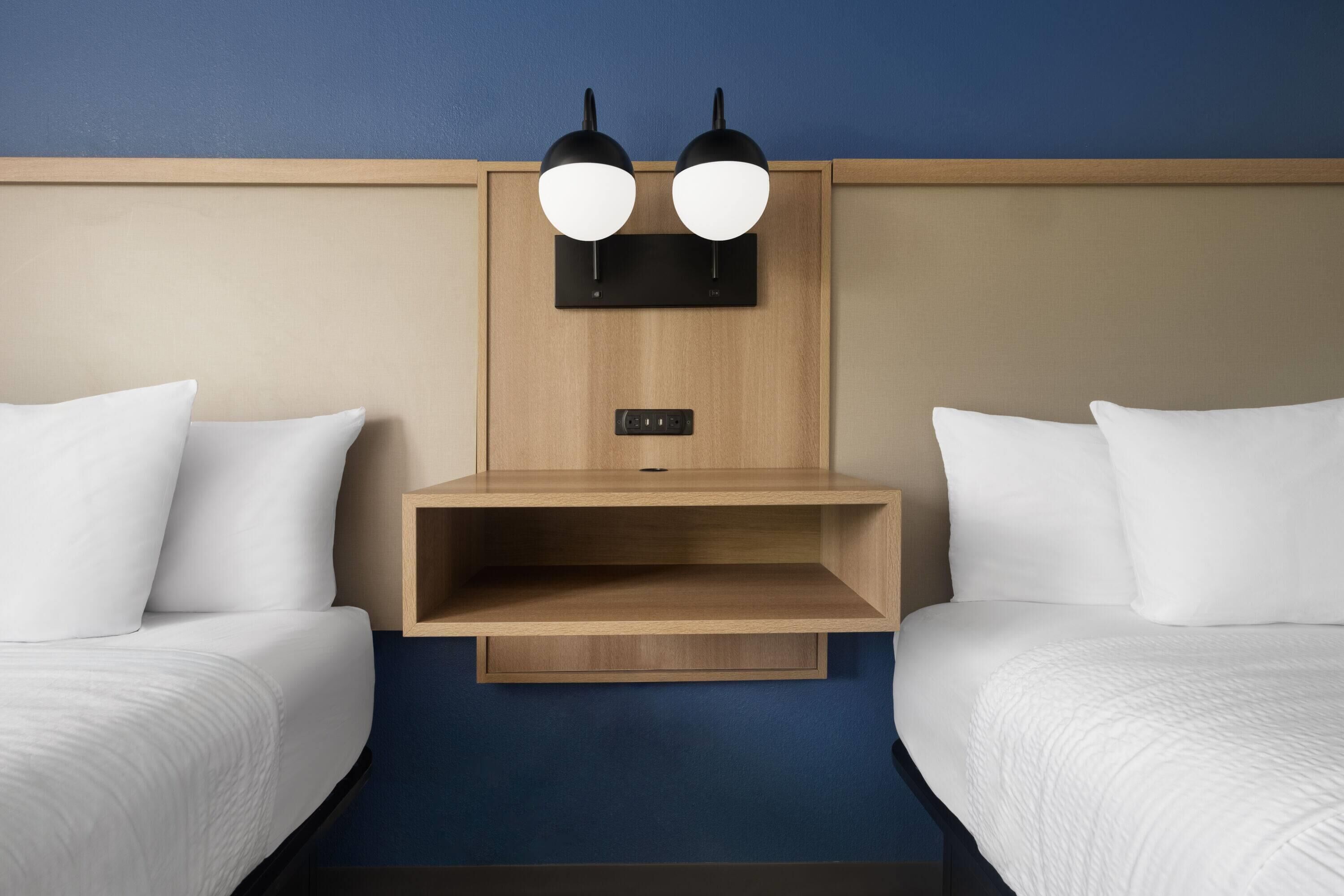 Ein Hotelzimmer mit zwei Einzelbetten, einem Holzkopfteil, einer eingebauten Ablage und einer Wandleuchte.