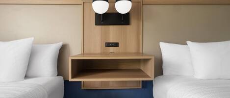 A hotel room with two single beds, a wooden headboard, a built-in shelf, and a wall-mounted light fixture.