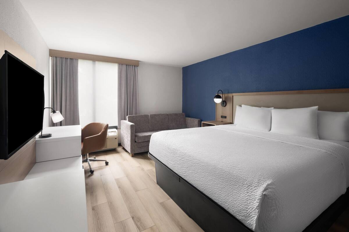 A hotel room with a large bed, a desk with a TV, a chair, and a window with curtains.