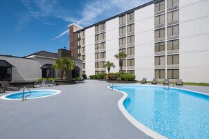 Zona de piscina con sillones de descanso y un edificio con amplias ventanas.