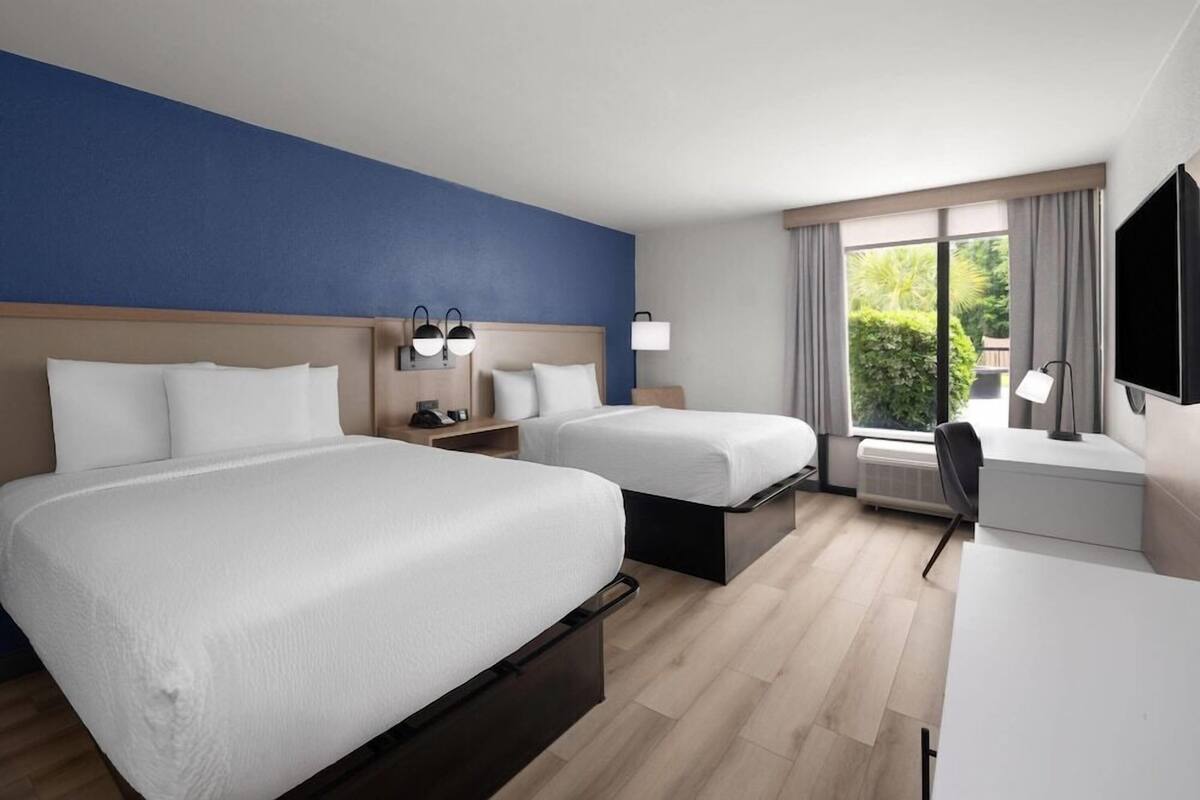 A hotel room with two beds, a desk, a chair, a TV, and a window with curtains.