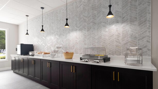A modern kitchen with a white countertop, black cabinets, and a herringbone-patterned backsplash. There are pendant lights, a coffee machine, and a fruit bowl on the counter. - La Quinta Inn & Suites by Wyndham Myrtle Beach (Myrtle Beach)