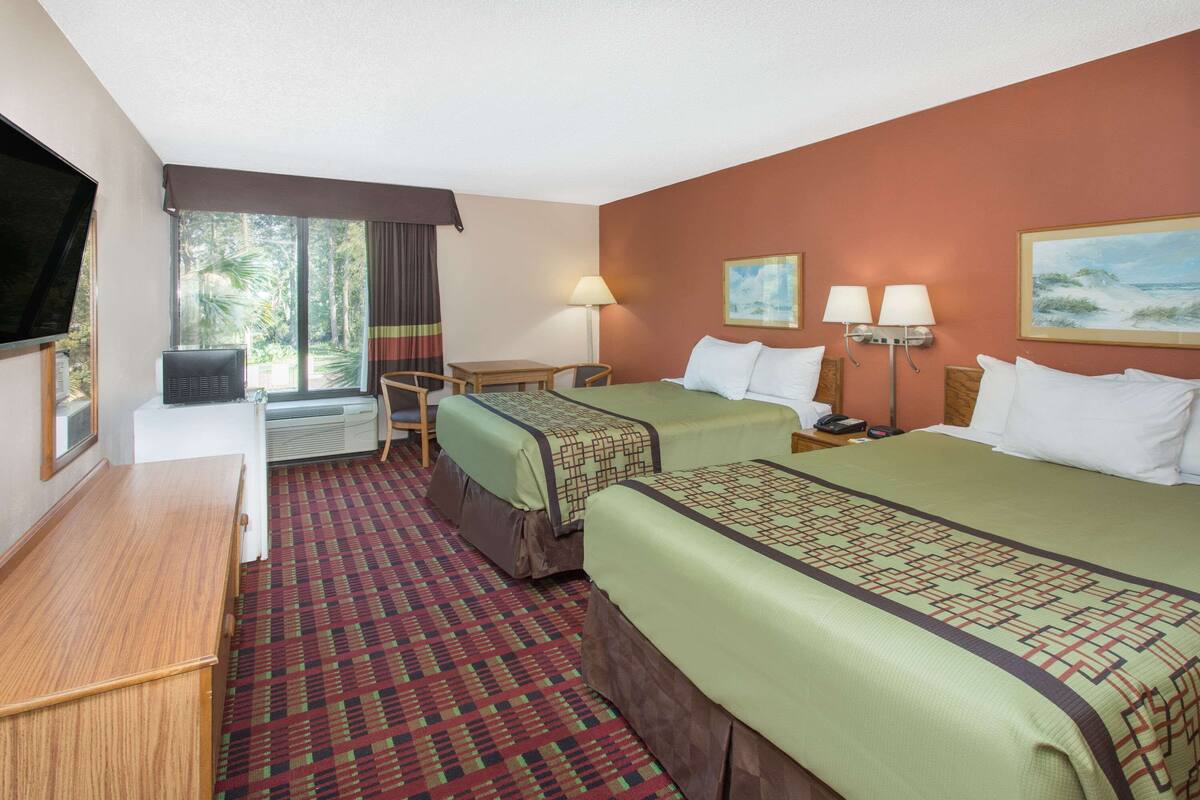 A hotel room with two beds, a desk, a TV, and a window with curtains.